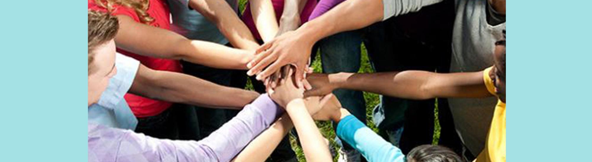 Circle of people with extended arms, hands upon hands.