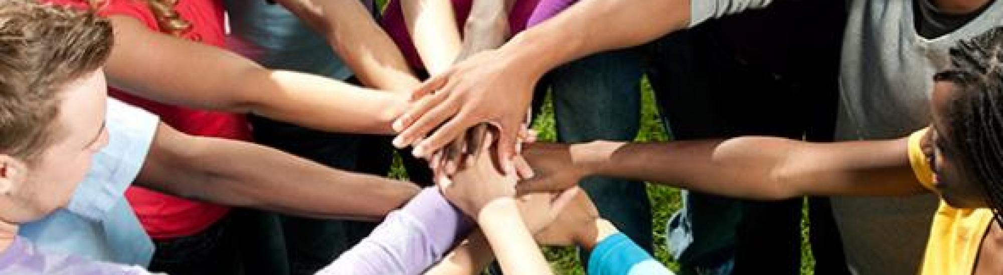 Circle of people of various races placing their hands upon each others hands.