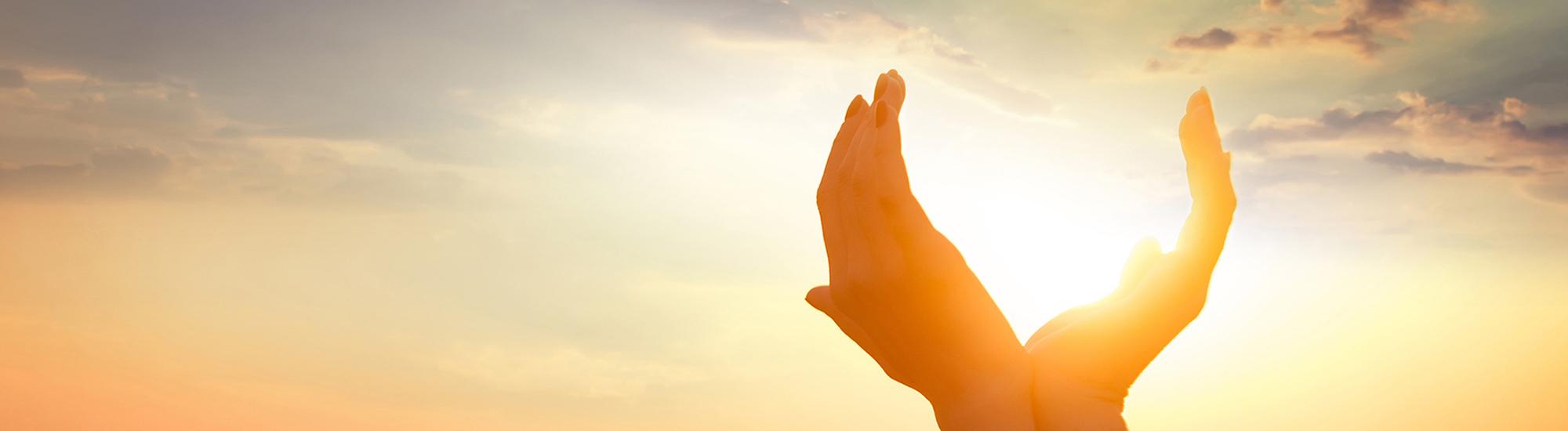 View of the sky with two open hands holding the light of the sun.